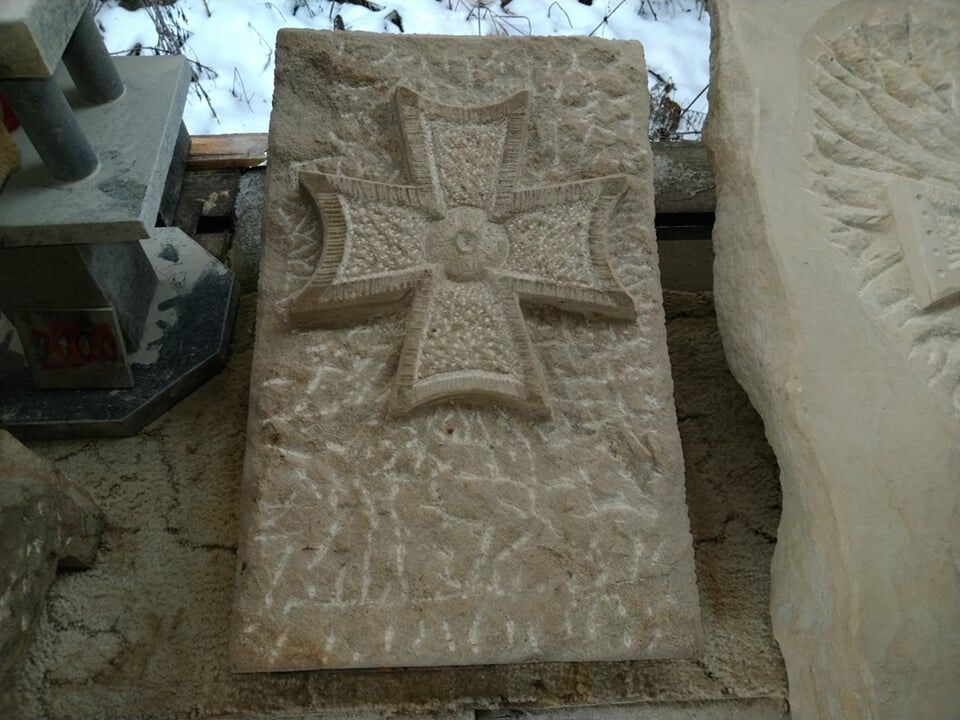 Kříž z přírodního pískovce, který je jako plastika vytvořený na obdélníkové desce.
