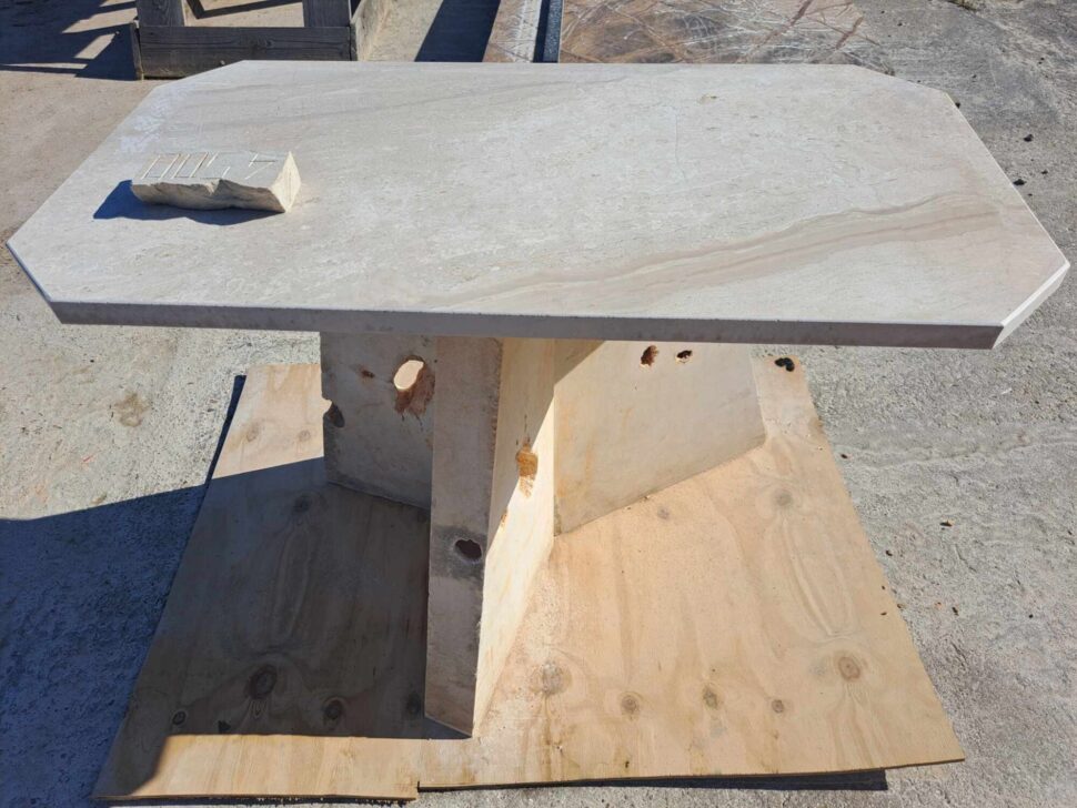 Stůl z vápence, který má atypicky tvarovanou tří bokou stolovou nohu.
